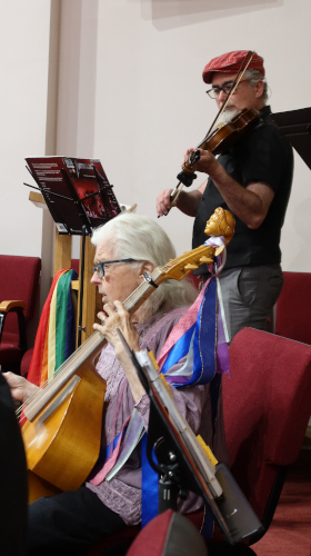 A woman playing a viola de gamba, with a violinist in the background.